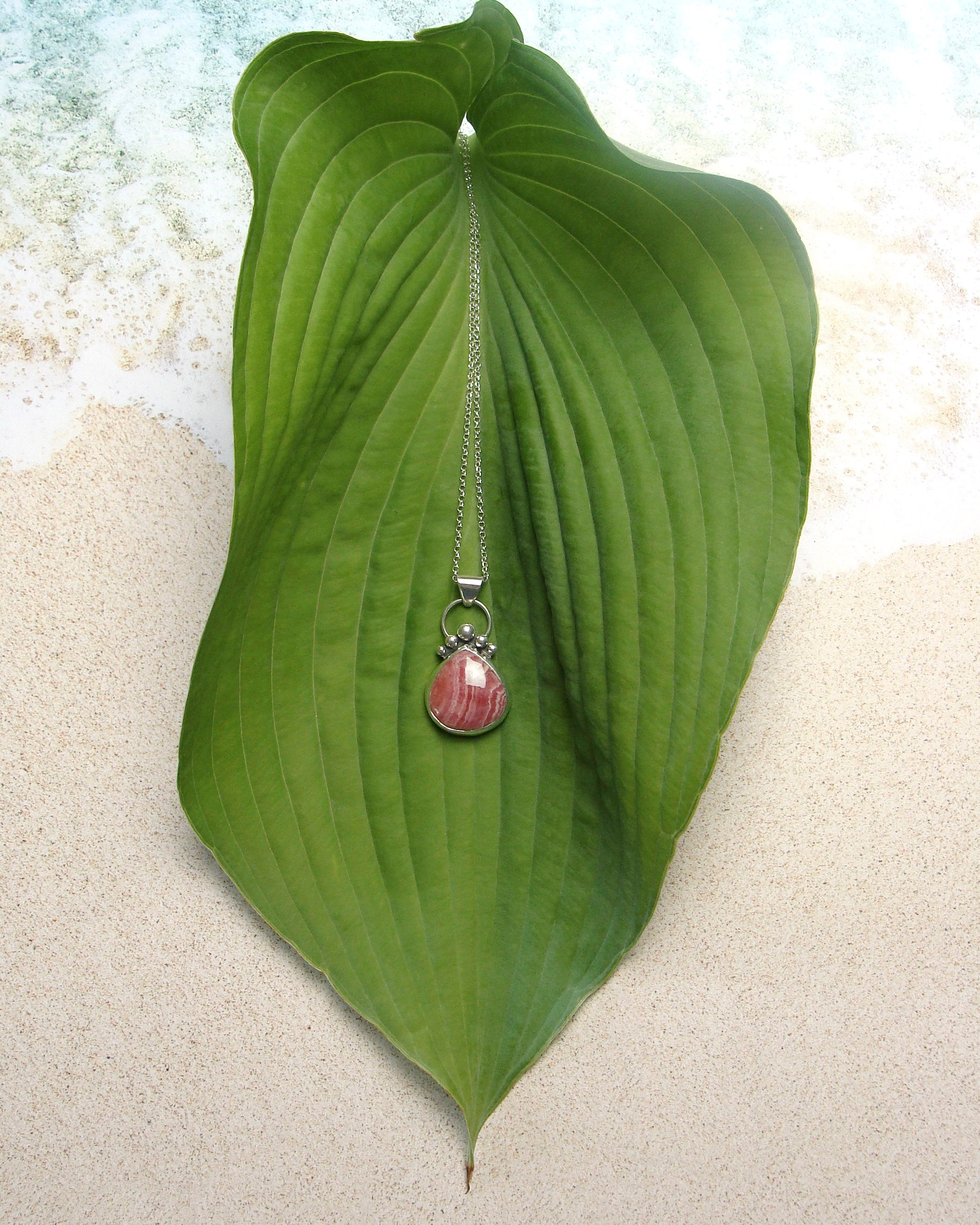 pear-shaped rhodochrosite pendant on leaf flatlay