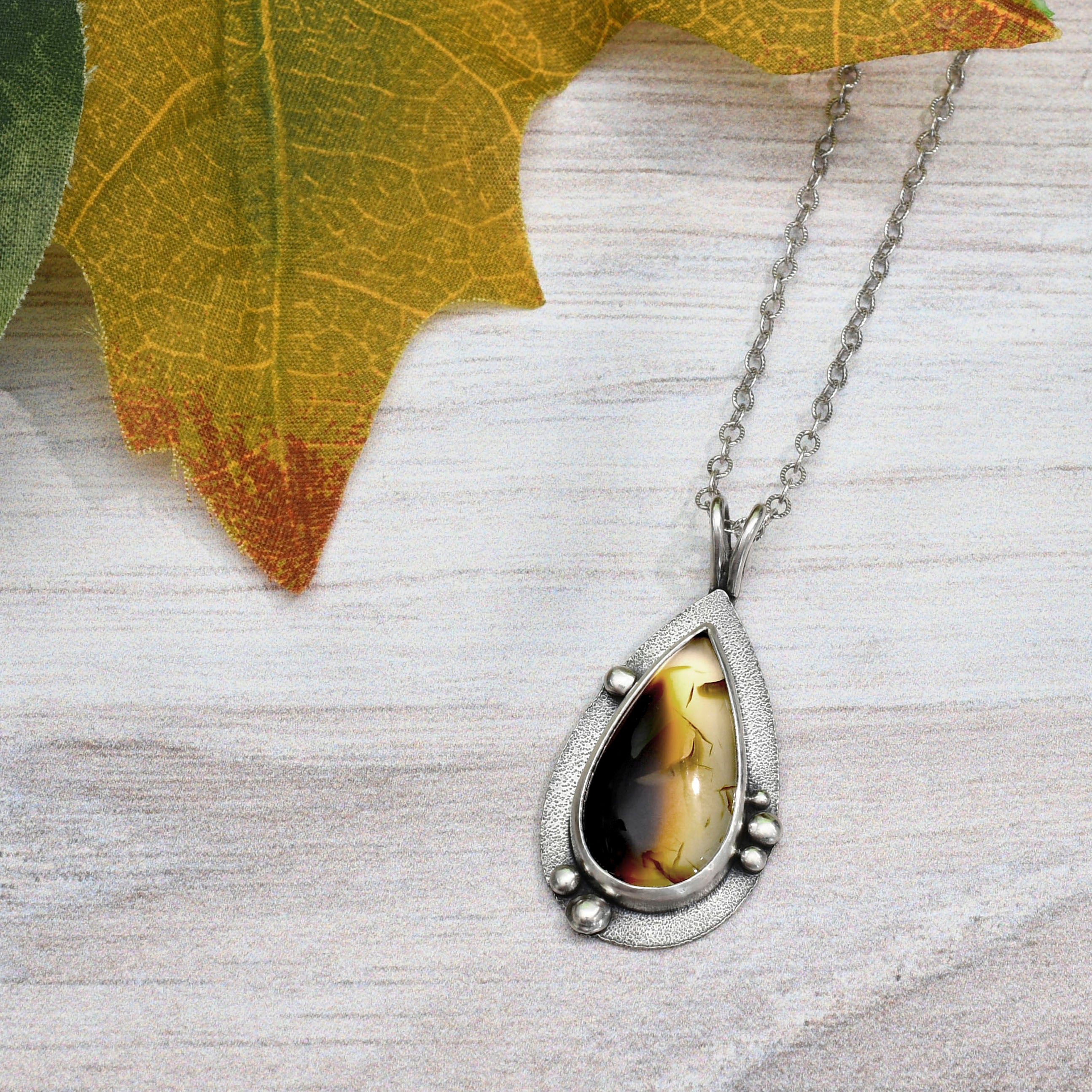 montana agate teardrop pendant with chain - flatlay with leaves
