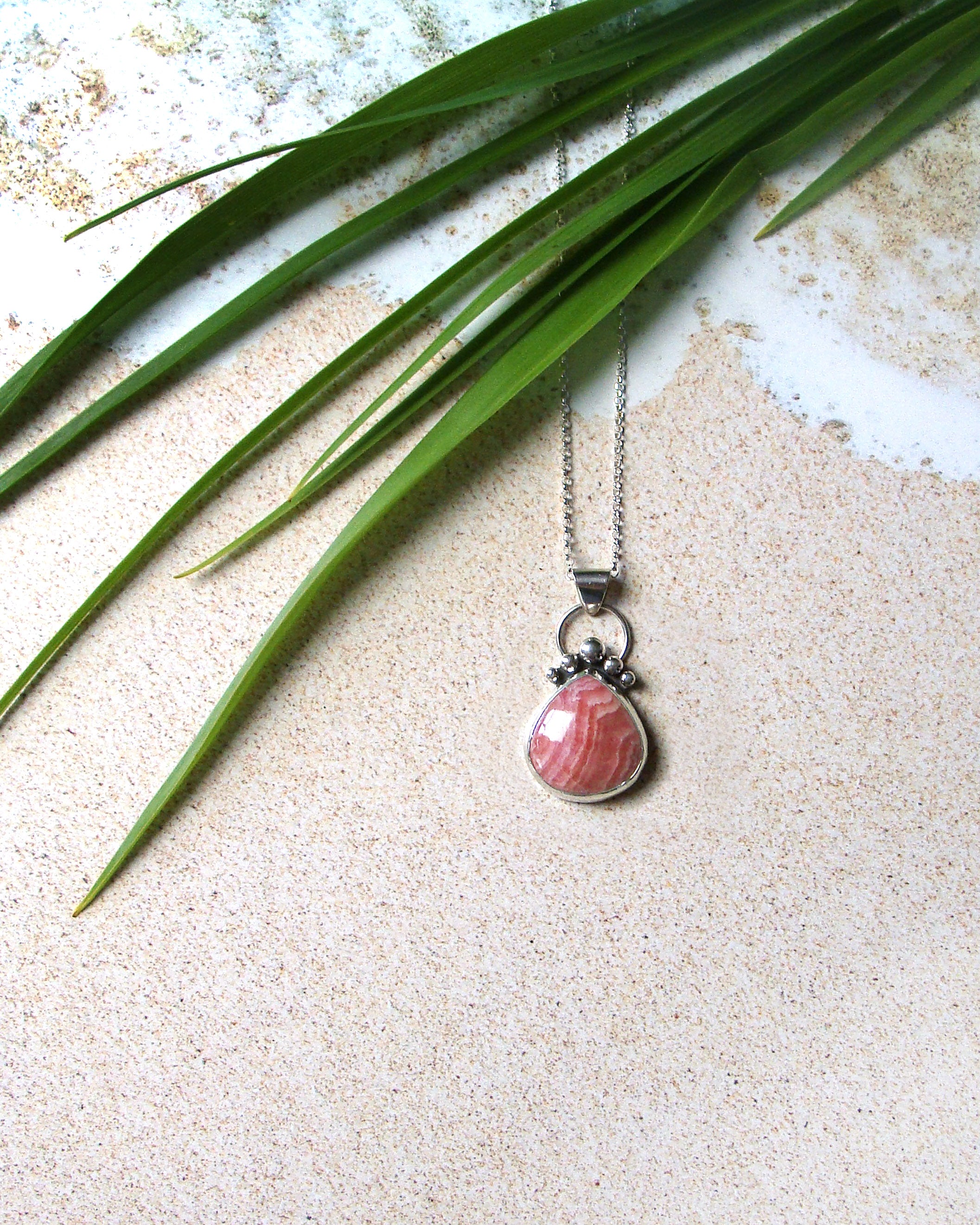 pear-shaped rhodochrosite pendant - flat lay with palm leaves