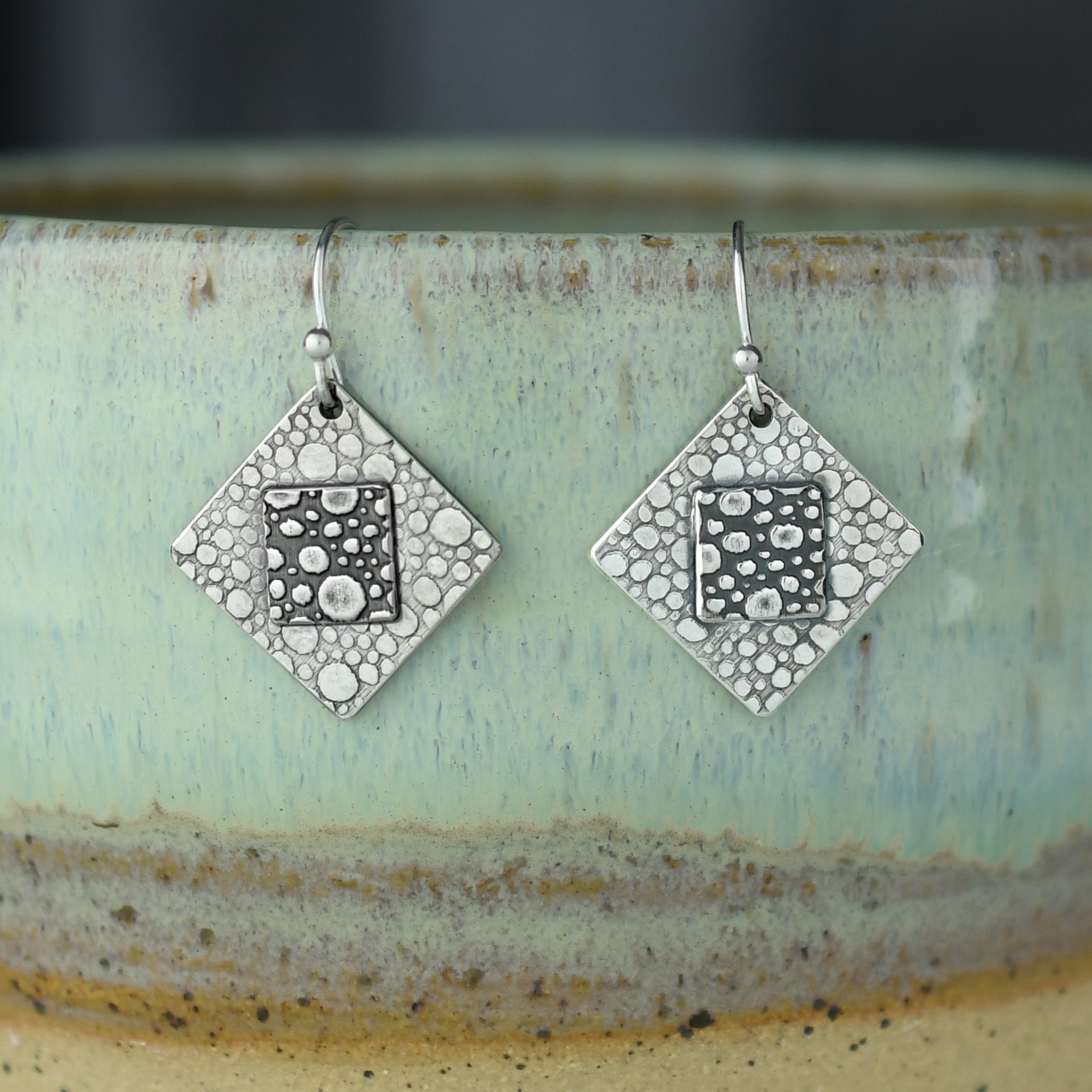 square silver earrings with pebble texture on prop